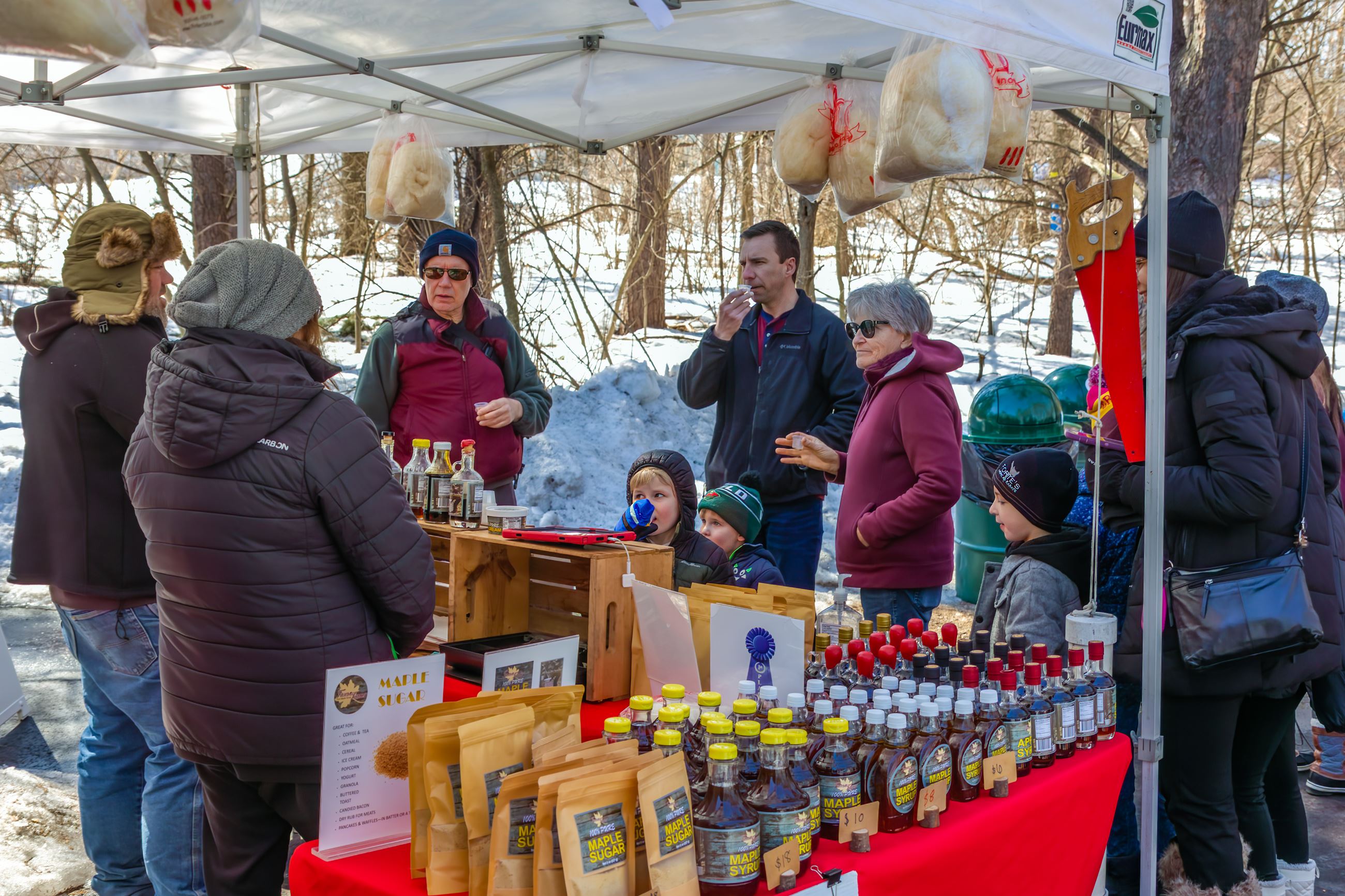 Visitors sampling maple syrup at Faxon Farms booth. Booth is stocked with maple syrup and sugar.